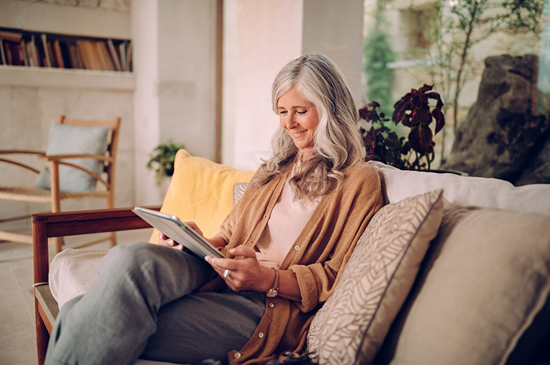 A senior woman with hearing aids reads the Colorado Ear Care Blog on a tablet