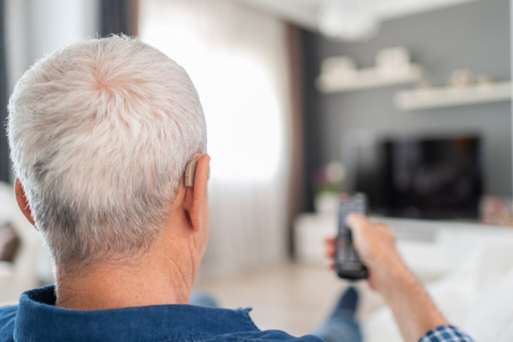 Man using a hearing aid while watching TV with a remote control