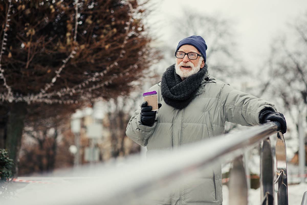 A senior man walks on a snowy road holding a railing