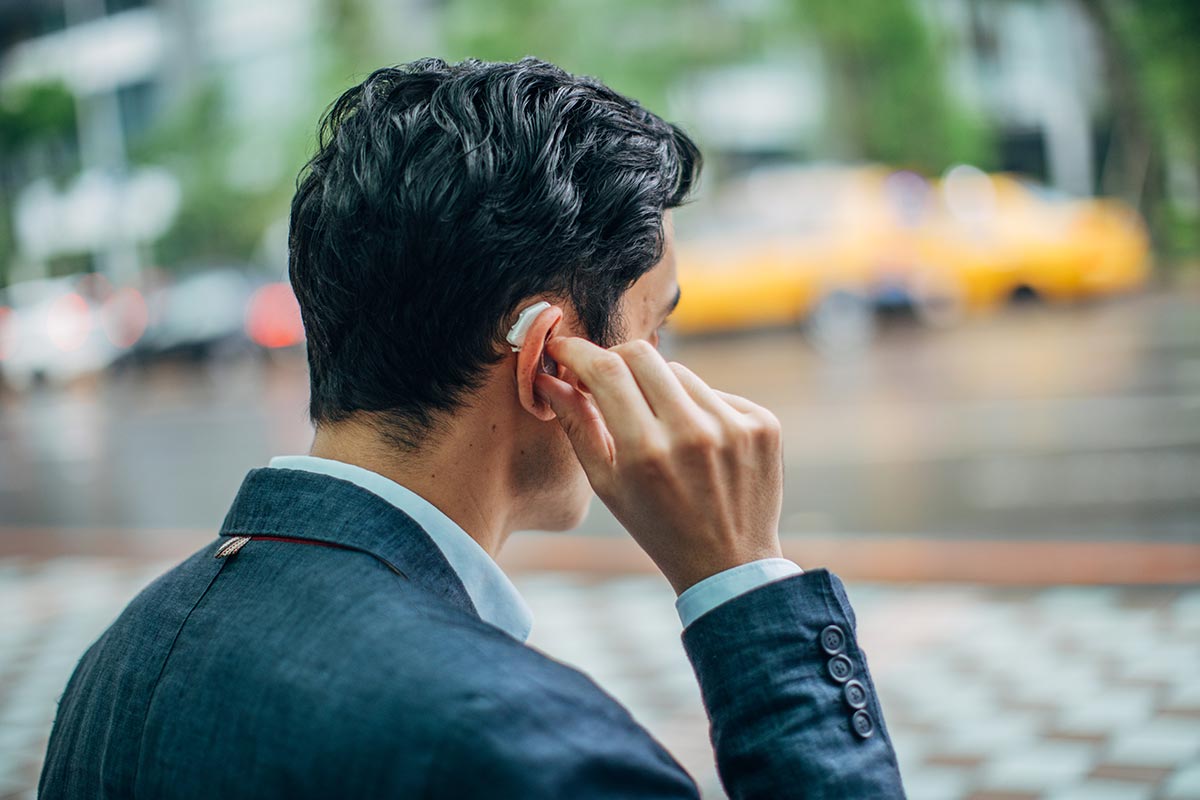 A young businessman adjusting his hearing aid while walking on a city street.