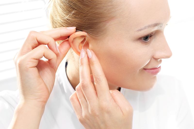 young woman places hearing aid on her ear
