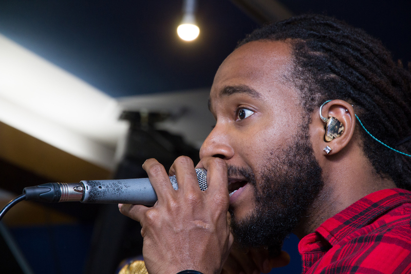 A close-up picture of a vocalist who is singing into a microphone while wearing in-ear monitors to protect his hearing and experience better sound quality