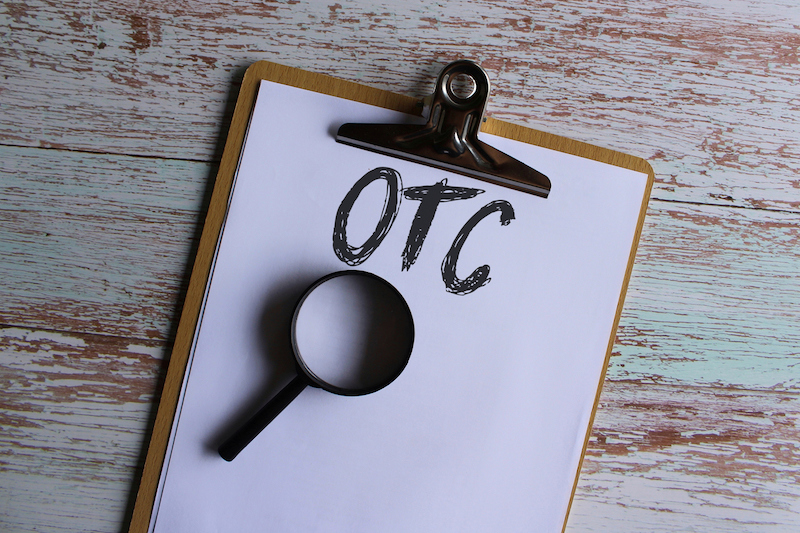Top view image of paper on a clipboard with text saying "OTC" and a magnifying glass lying below it.