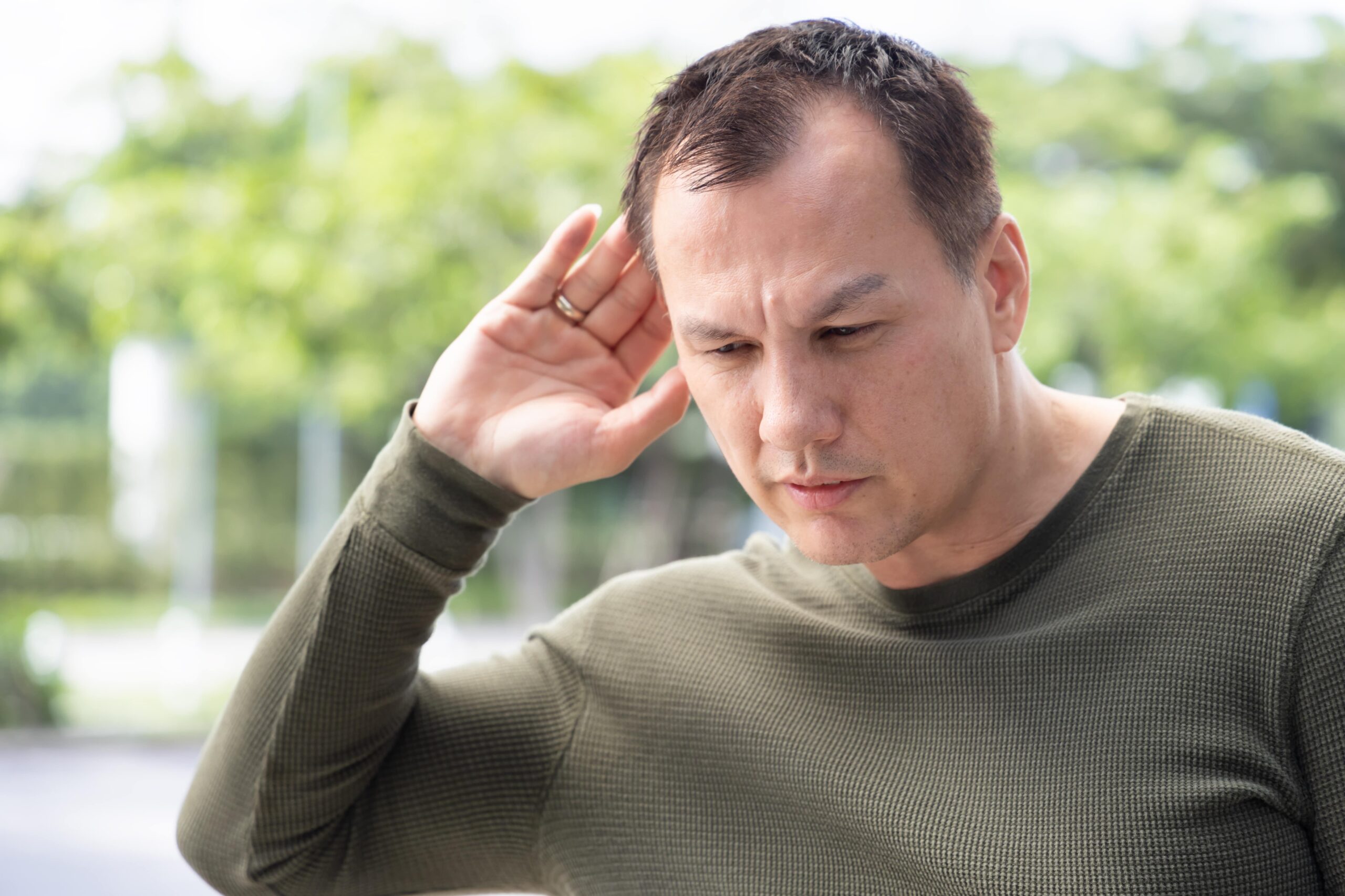 Man outside struggling with hearing loss.