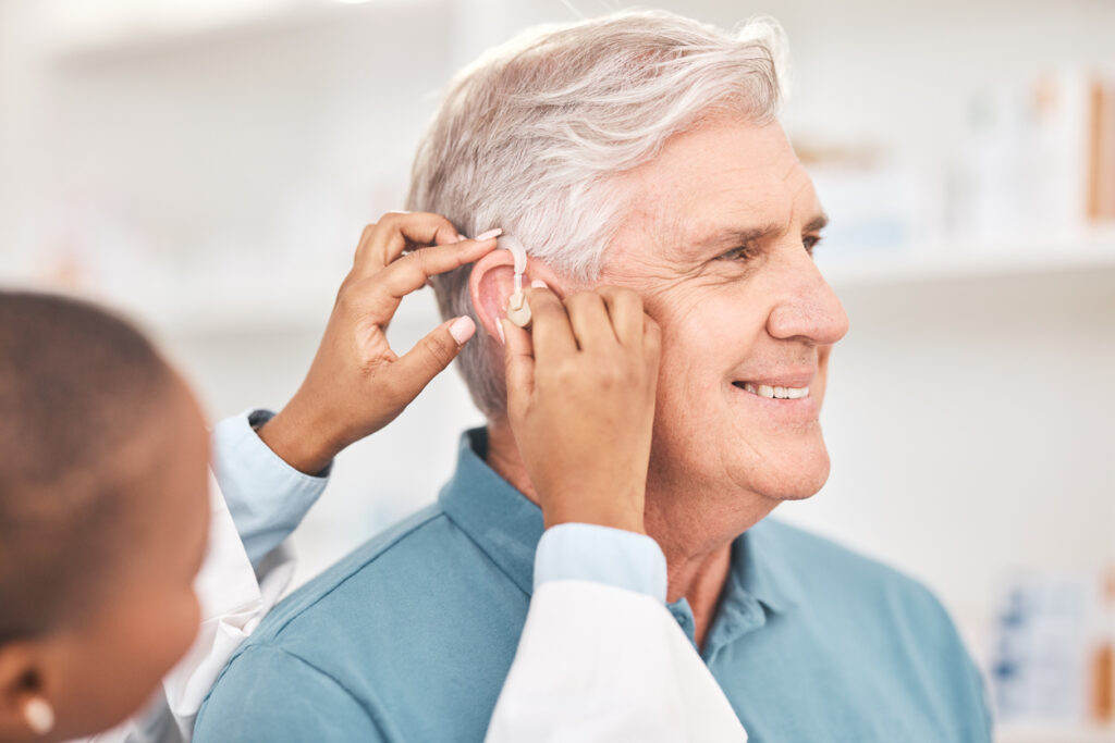 Smiling man having hearing aid checked by audiologist