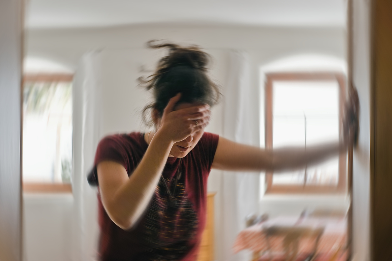 Woman holding her head and leaning on a wall, experiencing dizziness from vertigo.