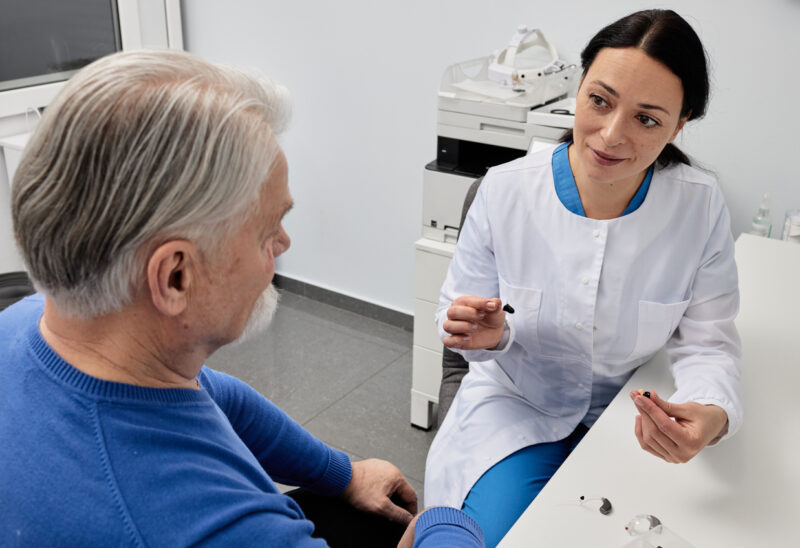 Audiologist explaining hearing aid options to an older patient during a consultation.