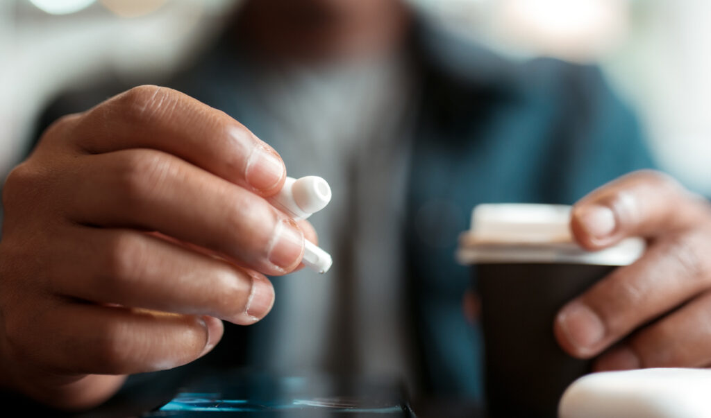 Close-up of a person holding an AirPod, symbolizing new hearing assistance features.