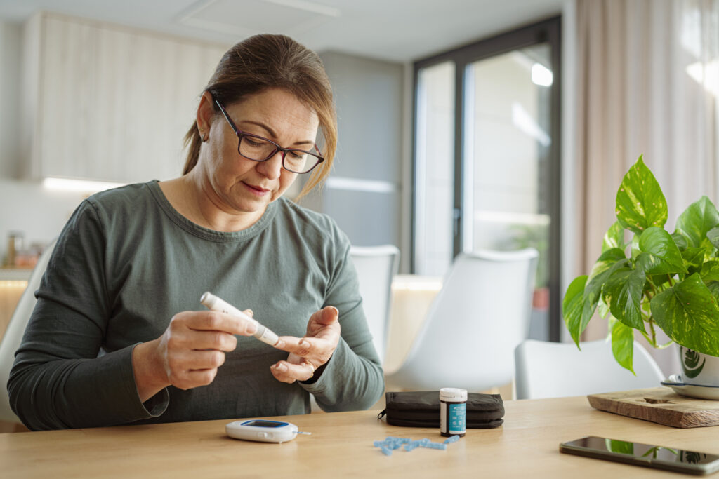 Middle-aged woman with glasses checking her blood sugar level using a glucometer at home.