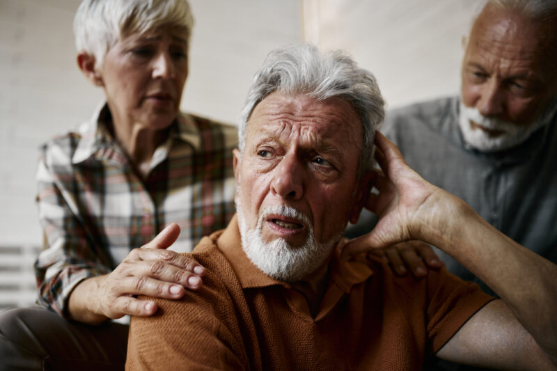 lder man struggling to hear with concerned friends offering support, symbolizing the challenges of progressive hearing loss.