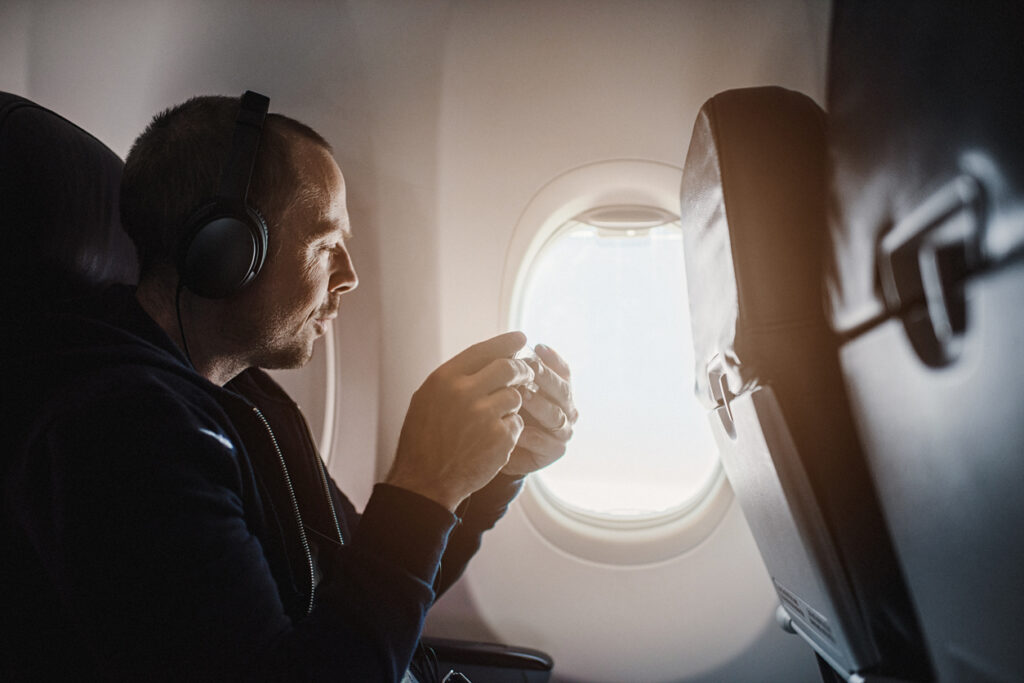 Man wearing noise-cancelling headphones on an airplane looking out the window