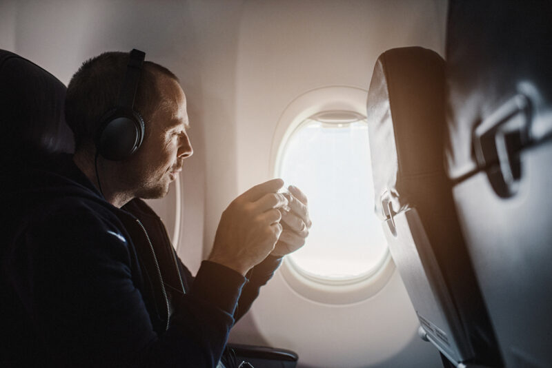 Man wearing noise-cancelling headphones on an airplane looking out the window